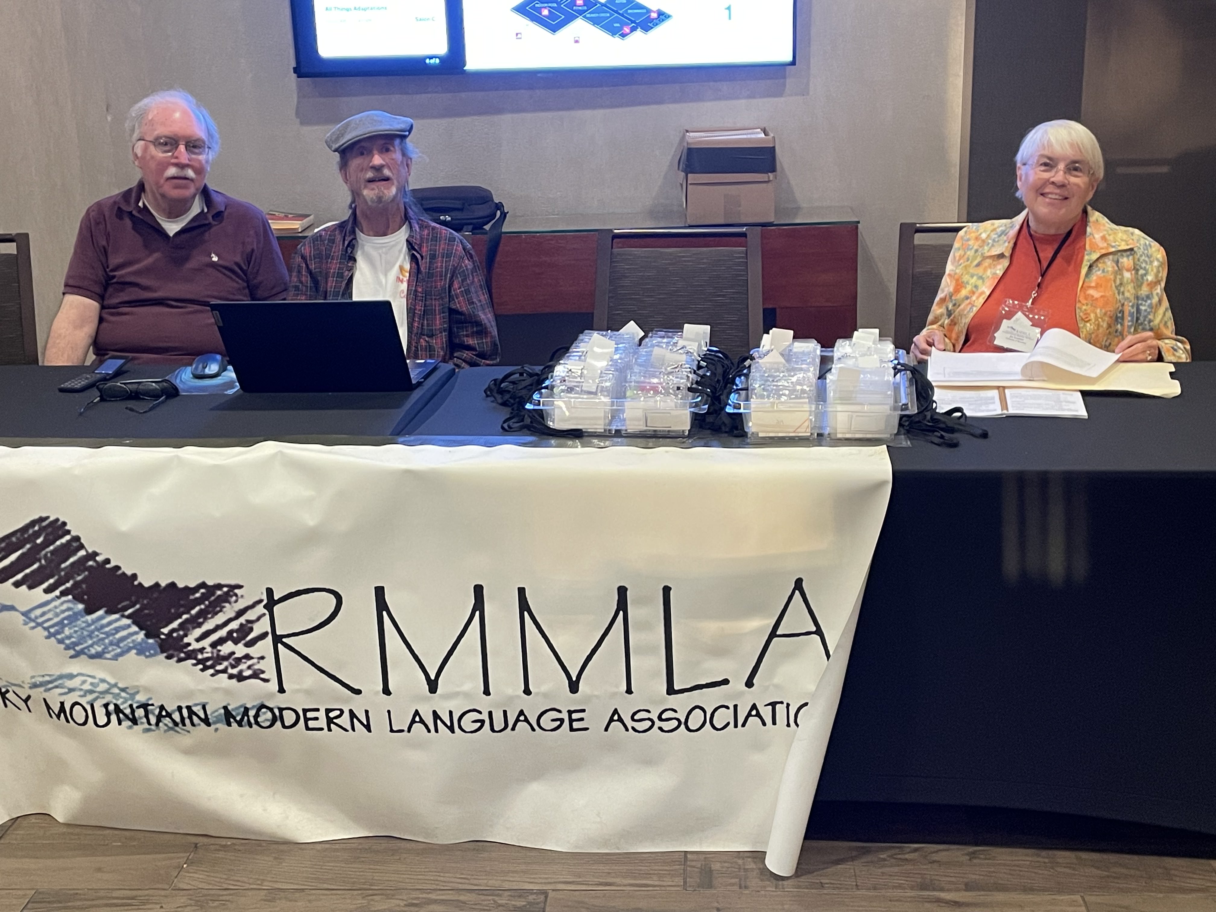 Three people stand at the 2023 Registration table for the RMMLA Convention